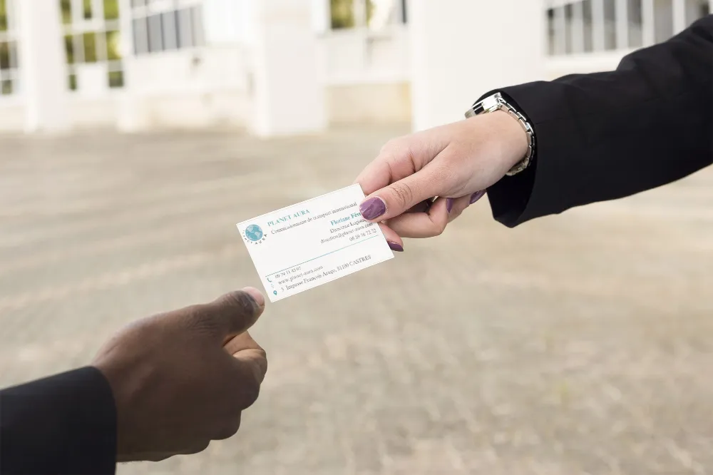 Deux personnes échangeant une carte de visite de Planet Aura, symbolisant une collaboration professionnelle dans le domaine de la logistique et de l’exportation de vins et champagnes.