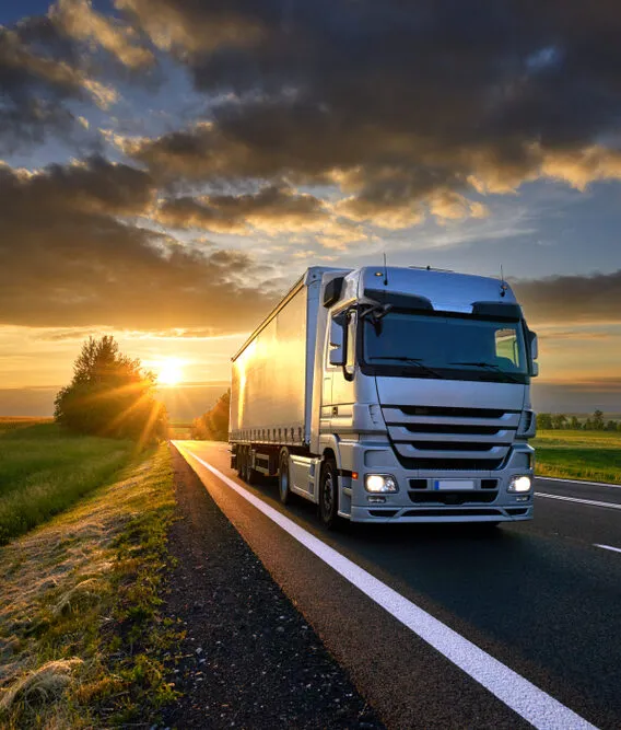 Camion de transport roulant sur une route au coucher du soleil, illustrant les expéditions nationales de vins et champagnes prises en charge par Planet Aura.