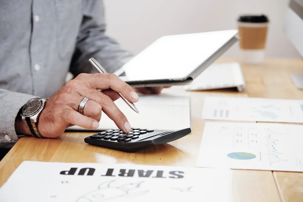 outils-numeriques-et-gestion-logistique-planet-aura_11zon Personne utilisant une calculatrice et une tablette pour la gestion des exportations de vins et champagnes chez Planet Aura.