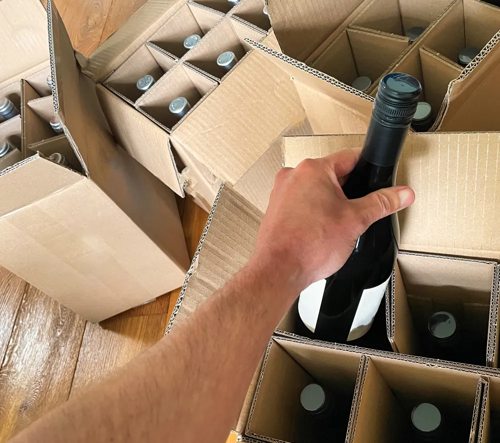 Préparation et mise en carton de bouteilles de vin dans un entrepôt de stockage logistique, illustrant les services de picking de Planet Aura.