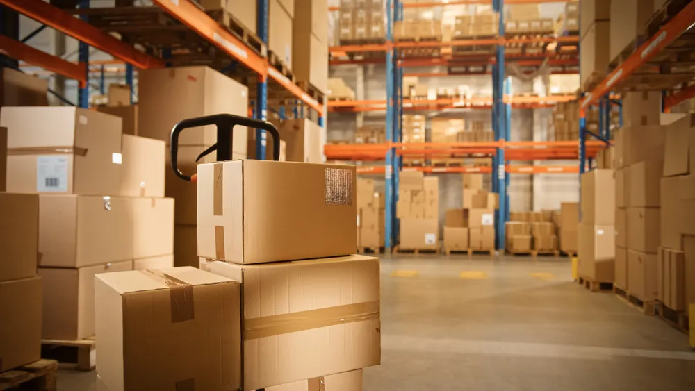 Entrepôt logistique avec des palettes et cartons empilés, illustrant les services de stockage et de picking offerts par Planet Aura.